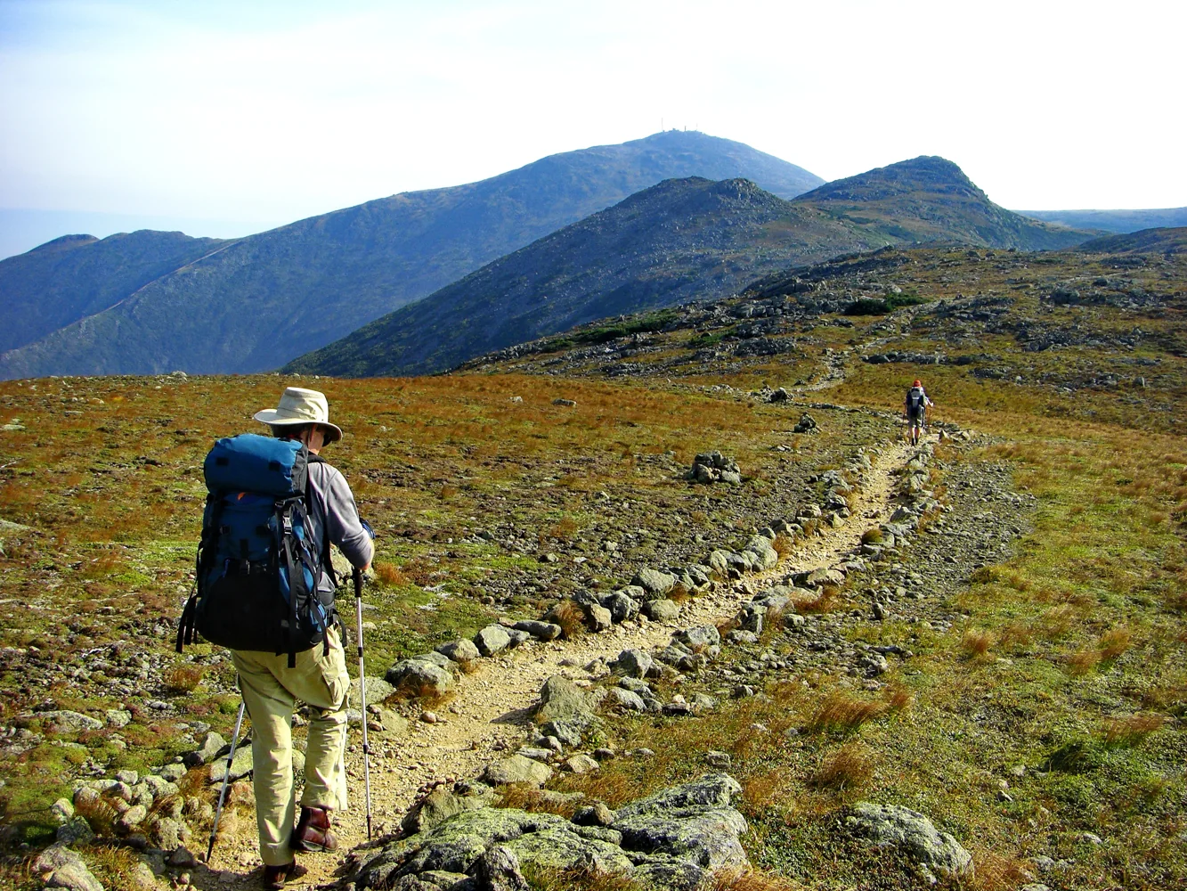 A backpacker follows the rocky Appalachian Trail across open ground in the White Mountains.